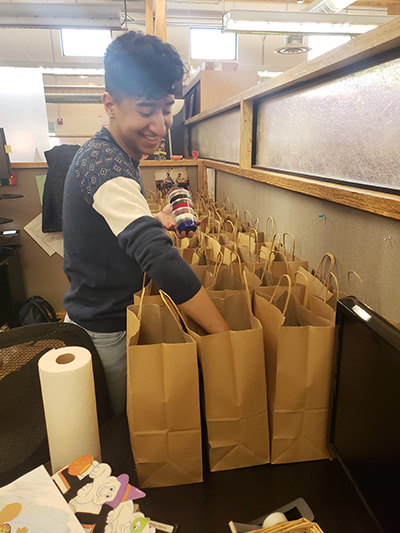 Ernesto prepares art kits for participants, putting tubs of paint into brown paper bags.