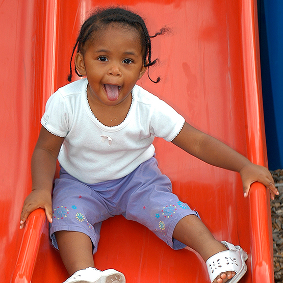 Young girl laughing while sliding down a playground slide.