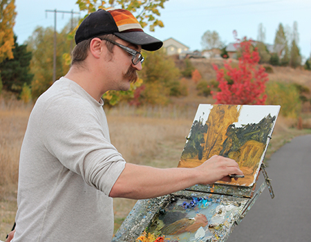 A man paints trees on a canvas outside.