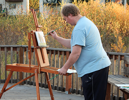 A man stands outside and paints on a canvas.