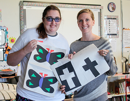 Two women hold their artwork up to pose for a picture.