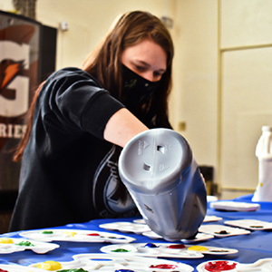 Suzanna wearing a mask and pouring paint into small containers for artAbility