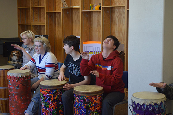 Mia and several other artAbility participants smile and bang on bongo drums.