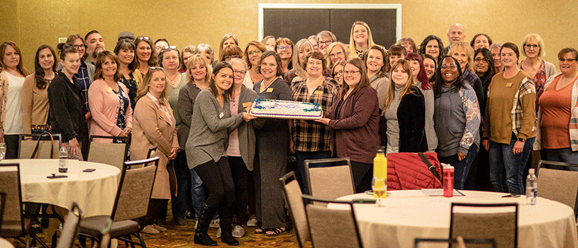 The IdahoSTARS team posing in a big group photo. Two people at the front are holding a large cake in celebration of the Project's 20th anniversary.