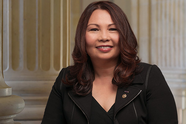 Tammy Duckworth, wearing a sleek black jacket and dress. She is smiling and looking directly at the camera.
