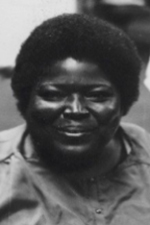 Johnnie Lacy is looking directly at the camera. She is a person of color and is smiling happily. She has close cut, natural hair and is wearing a button-up blouse.