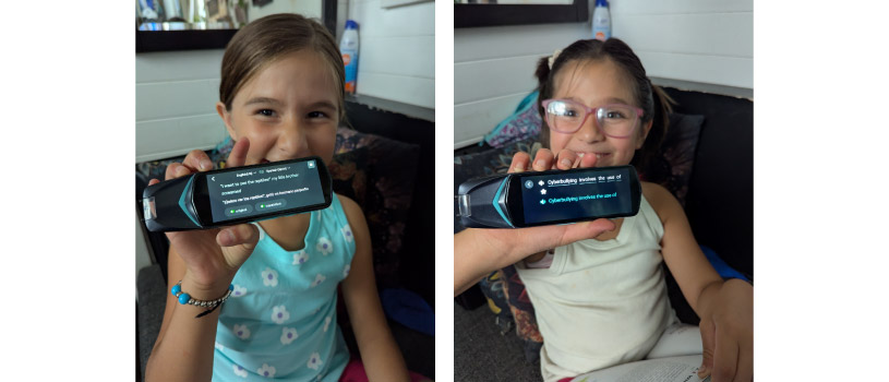 On the left: a young girl with long brown hair is smiling as she is holding up a reading pen to show the words on the screen. She is sitting on a bench with a book in her lap. ON the right: another young girls with short brown hair and glasses is holding up a reading pen to show the words on the screen. She is smiling happily.