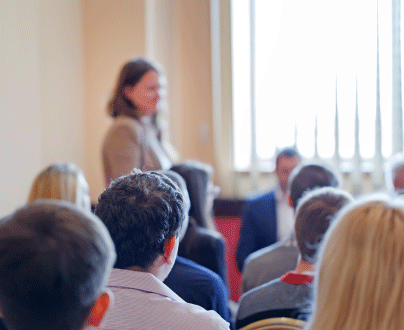A group of people sitting in a conference room, listening to a speaker at a conference.