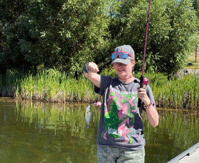 A young woman is holding up her fishing line, with a small fish hanging on the end of it. She is smiling as she looks at the fish.