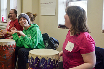 Two women laugh and play drums during a workshop.