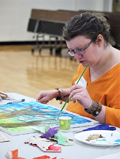 A participant thoughtfully paints a picture on a canvas.