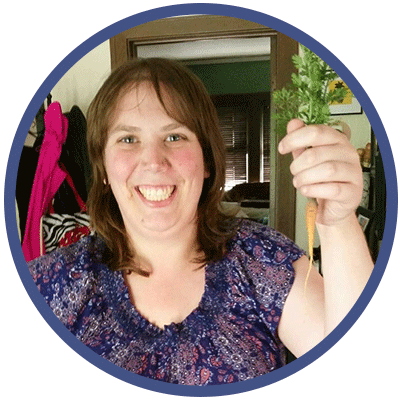 Caroline is smiling and proudly holding homegrown carrots up. She is wearing a purple top.