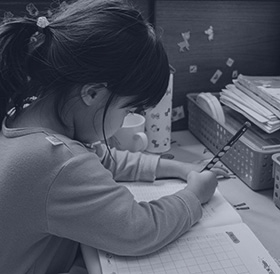 A young girl sits, working at a desk with a pencil and paper.
