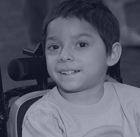 a young boy in an assistive wheelchair smiles at the camera.