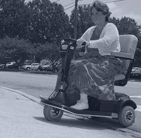 A woman rides a motor scooter down the sidewalk