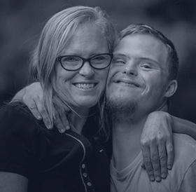 A mother and a son with down syndrome hug and smile at the camera.