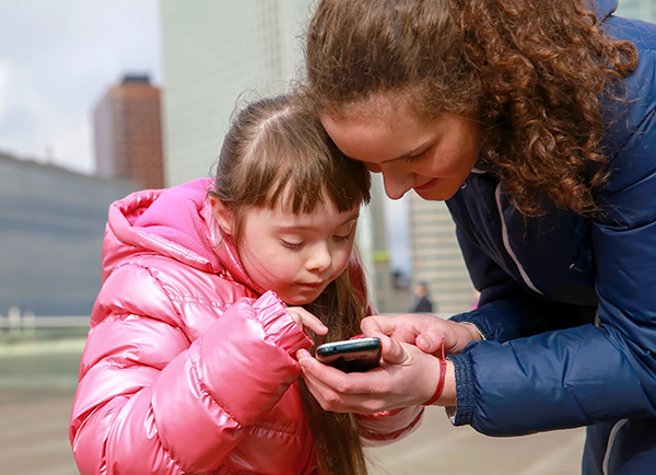 Young girl with autism looking at a smartphone with her mother.